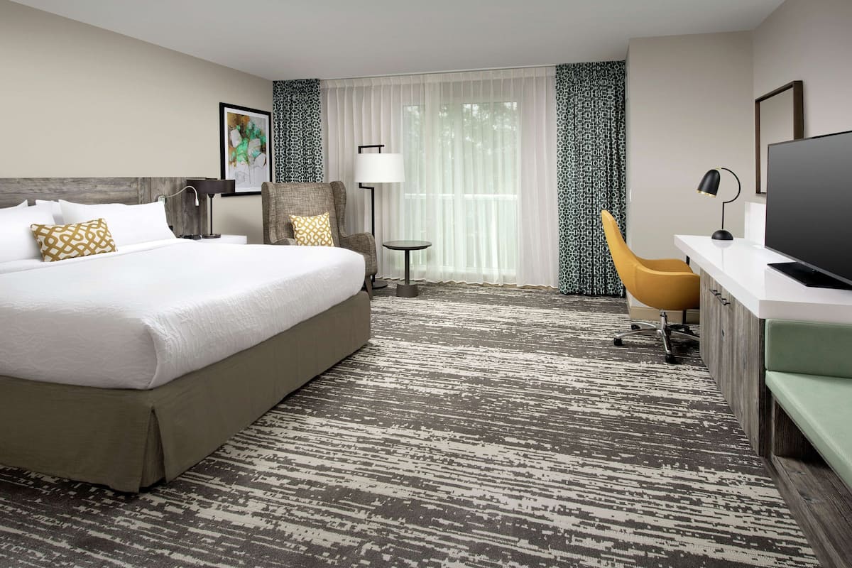 A hotel room with a large bed, a desk with a television, a chair, and a lamp.