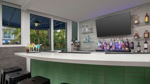 Un espace bar avec un comptoir recouvert de carreaux verts, un téléviseur à écran plat fixé au mur et une variété de bouteilles d’alcool exposées sur des étagères.