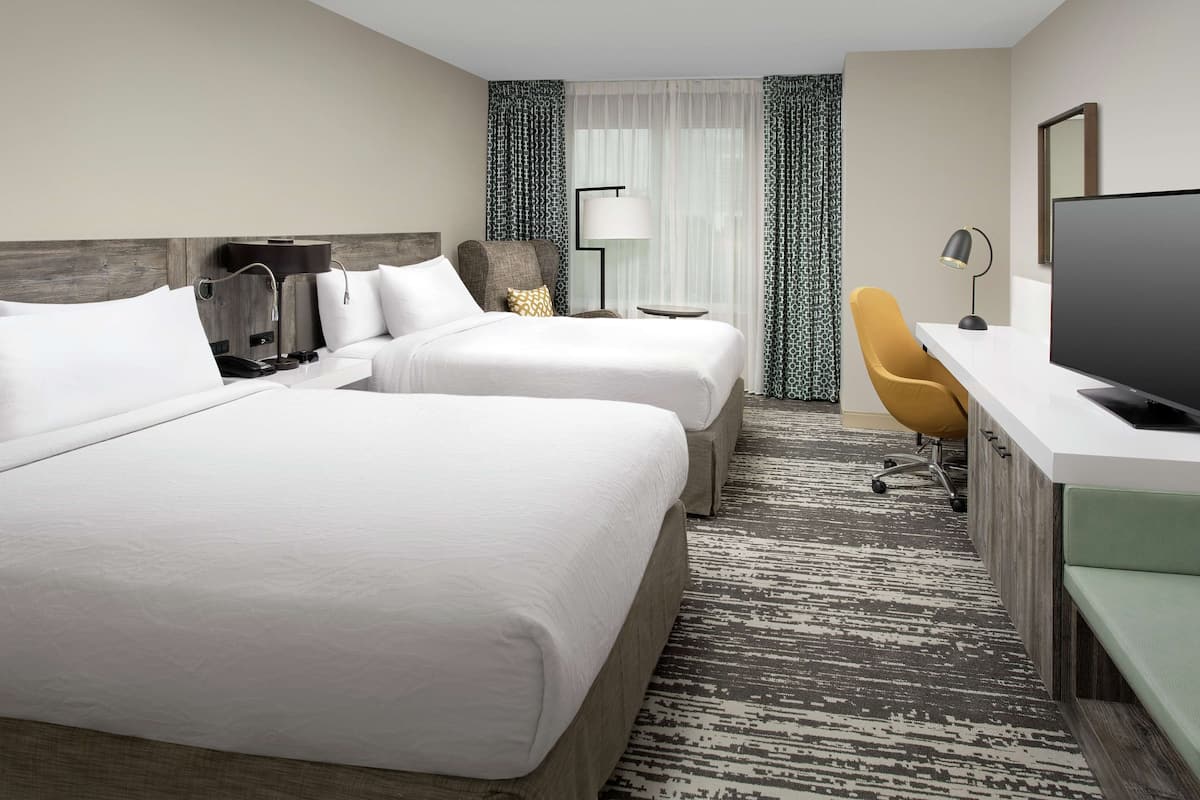 A hotel room with two beds, a desk with a computer, a chair, and a TV.