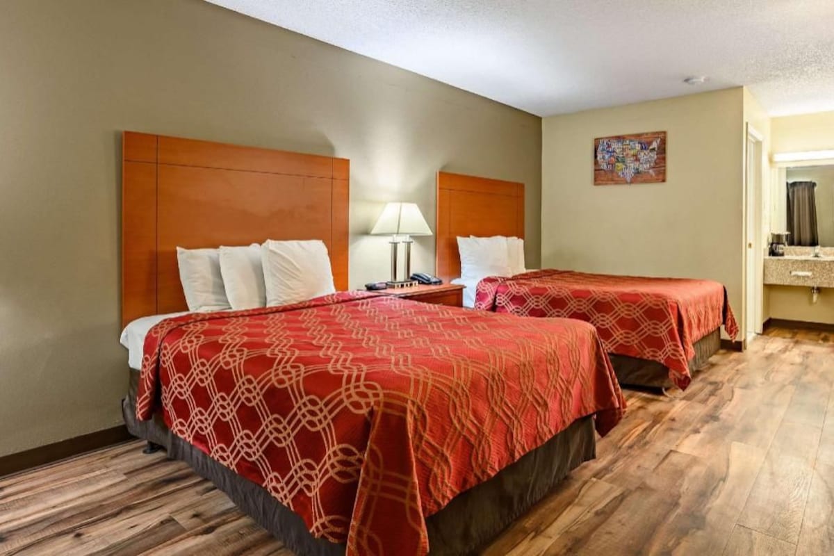 Habitación de hotel con dos camas, una mesita de noche, una lámpara, un espejo de baño y un adorno en la pared.