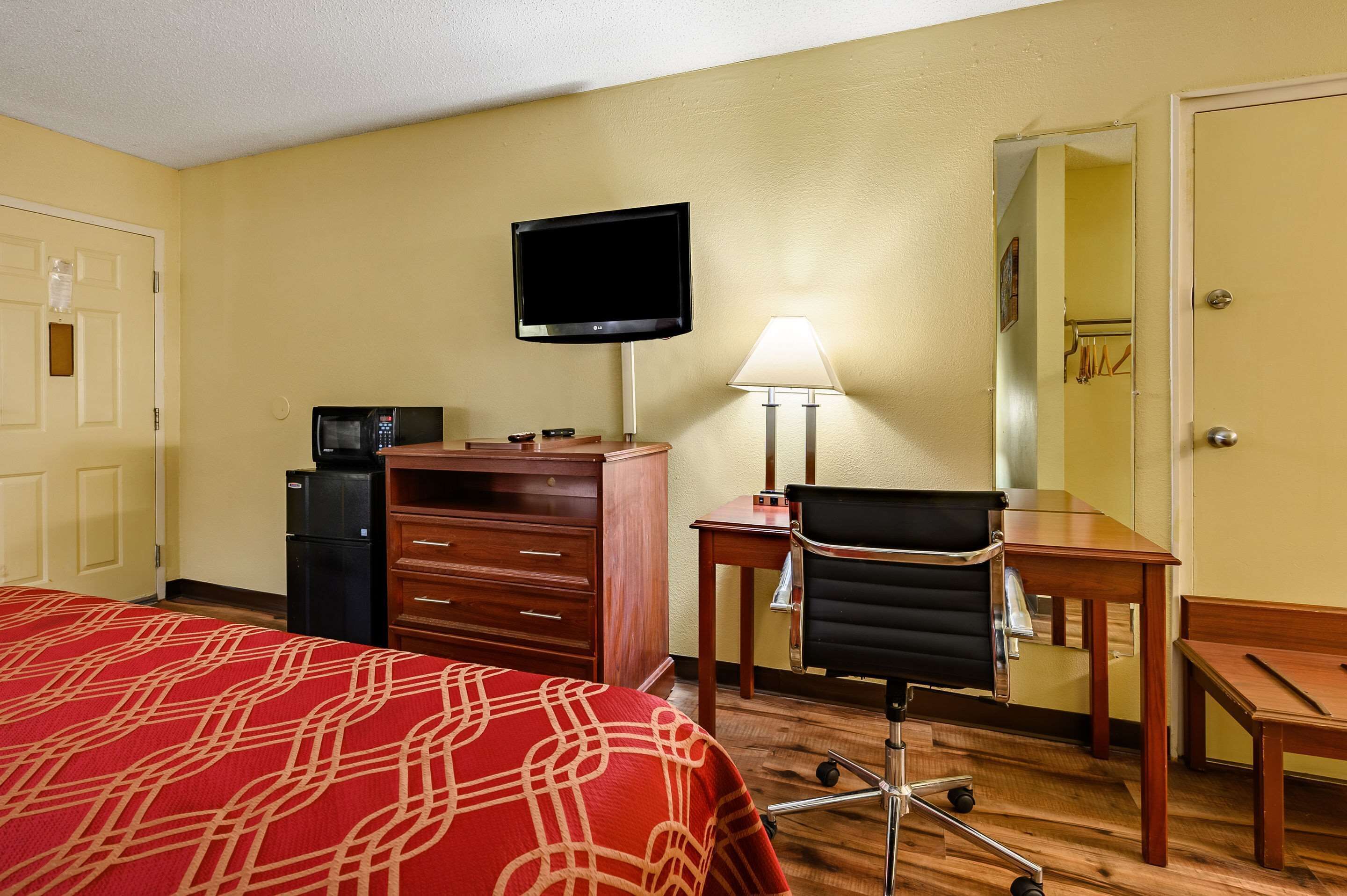 A hotel room with a bed, a desk, a chair, a television, a lamp, and a refrigerator.