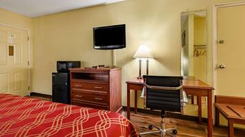 A hotel room with a bed, a desk, a chair, a television, a lamp, and a refrigerator.