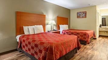 Une chambre d’hôtel avec deux lits, une table de chevet, une lampe, une œuvre d’art représentant une carte et une salle de bain visible à travers une porte ouverte.