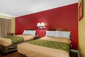 A hotel room with two beds, each with a green and beige bedspread, a red accent wall, and a nightstand with a lamp. - Econo Lodge Union City - Atlanta South (Union City)