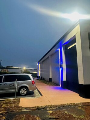 A building with a garage door, a parked SUV, and a sidewalk. - Econo Lodge Union City - Atlanta South (Union City)