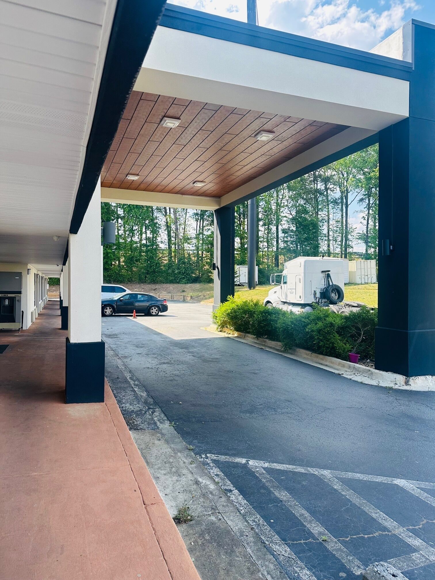 A covered parking area with a row of buildings, a paved road, and a trailer in the background.