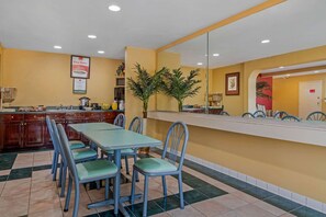 A dining area with a long table and chairs, a kitchen area with cabinets and appliances, and a mirror reflecting the room. - Econo Lodge Union City - Atlanta South (Union City)