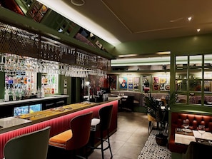 Una zona de bar con una barra larga, varios taburetes y una amplia variedad de botellas y vasos.