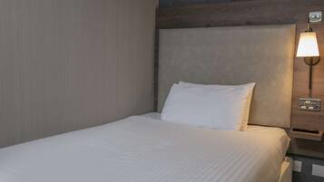 A neatly made bed with a white pillow and a wall-mounted light fixture above it.