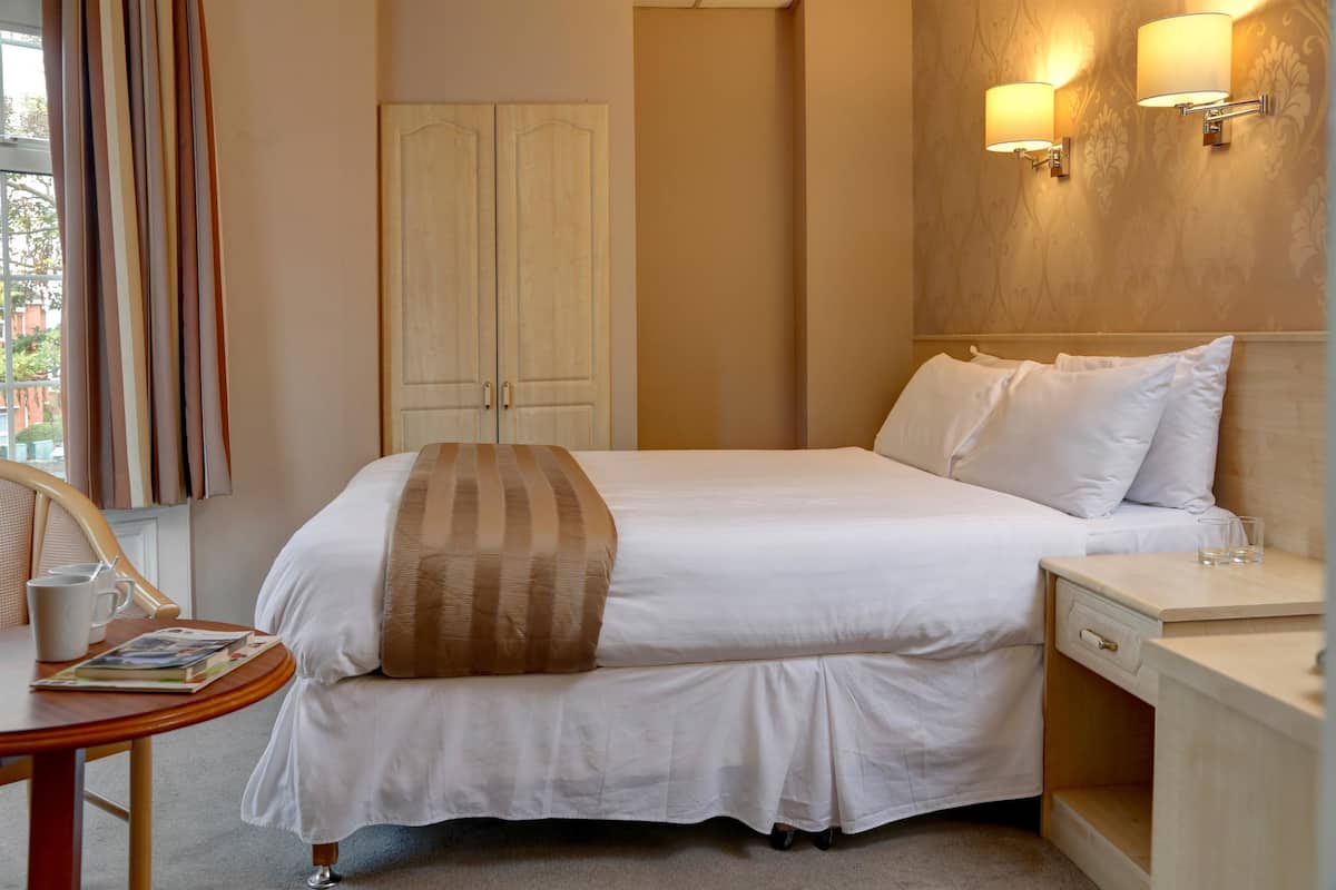 Une chambre d’hôtel avec un lit, une table de chevet, une lampe et une fenêtre avec des rideaux.