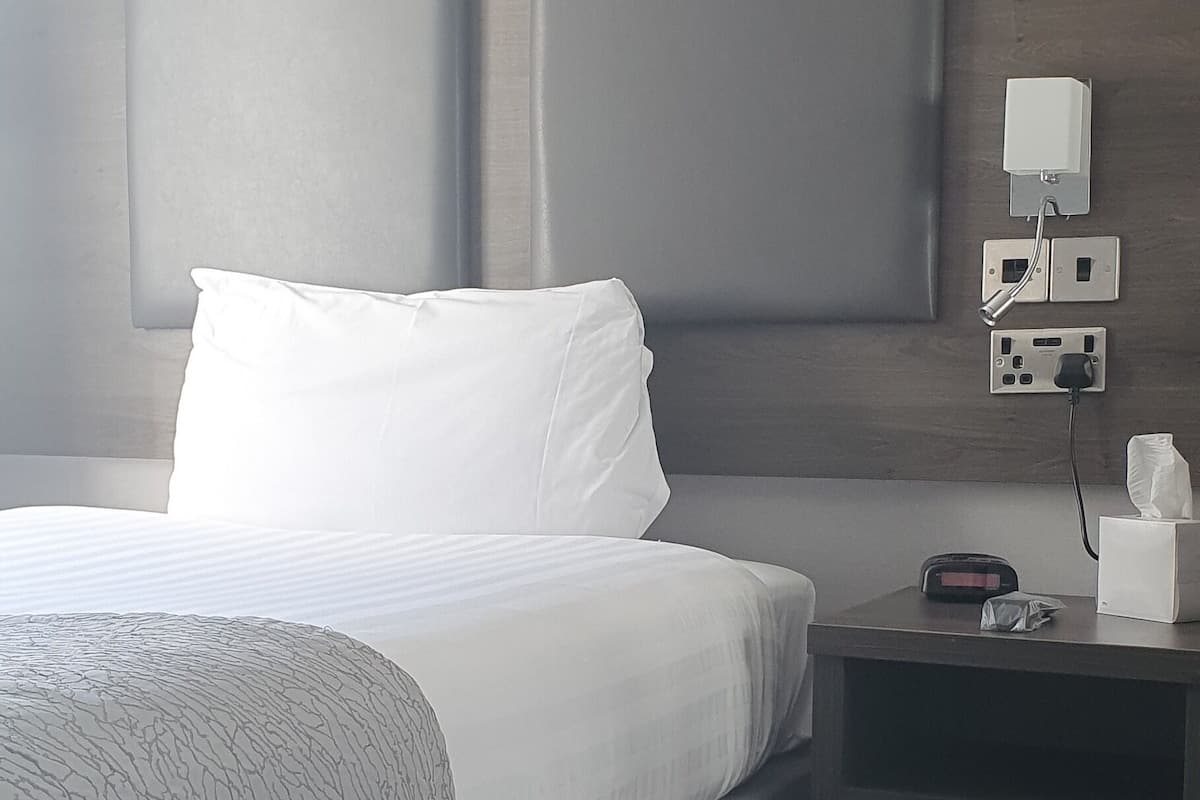 Une chambre d’hôtel avec un grand lit, une table de chevet avec une lampe et une prise de courant fixée au mur.