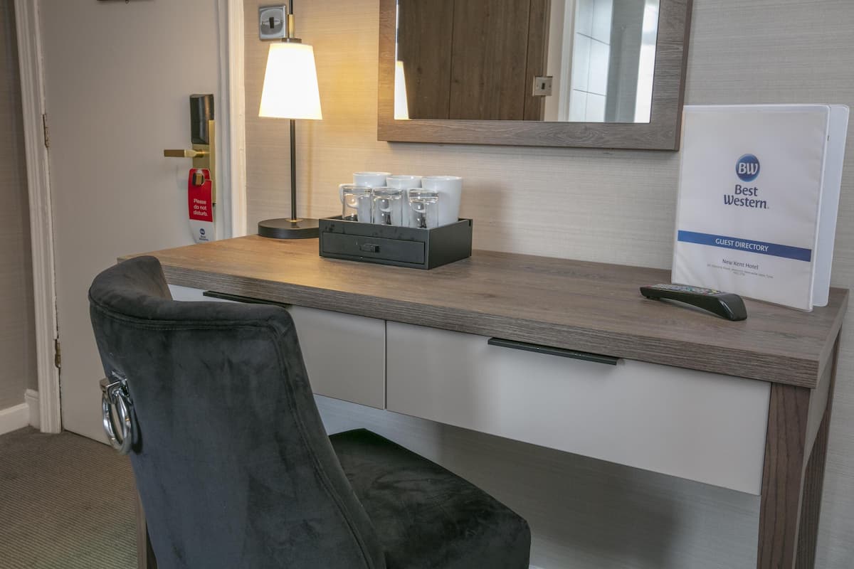 Un bureau d’hôtel avec une chaise, une lampe, un miroir, un annuaire des services de l’hôtel et un plateau avec des tasses et des verres.