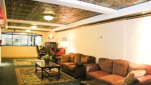 A lobby with a patterned carpet, leather sofas, a coffee table, and a ceiling with a decorative design.