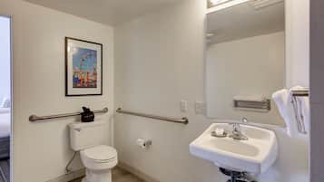 Un baño con inodoro, bidé, lavamanos, barras de apoyo y espejo.
