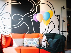 A modern living room with a sofa, colorful pillows, and a dog with balloons. - Ibis Aix en Provence Hotel (Aix-en-Provence)