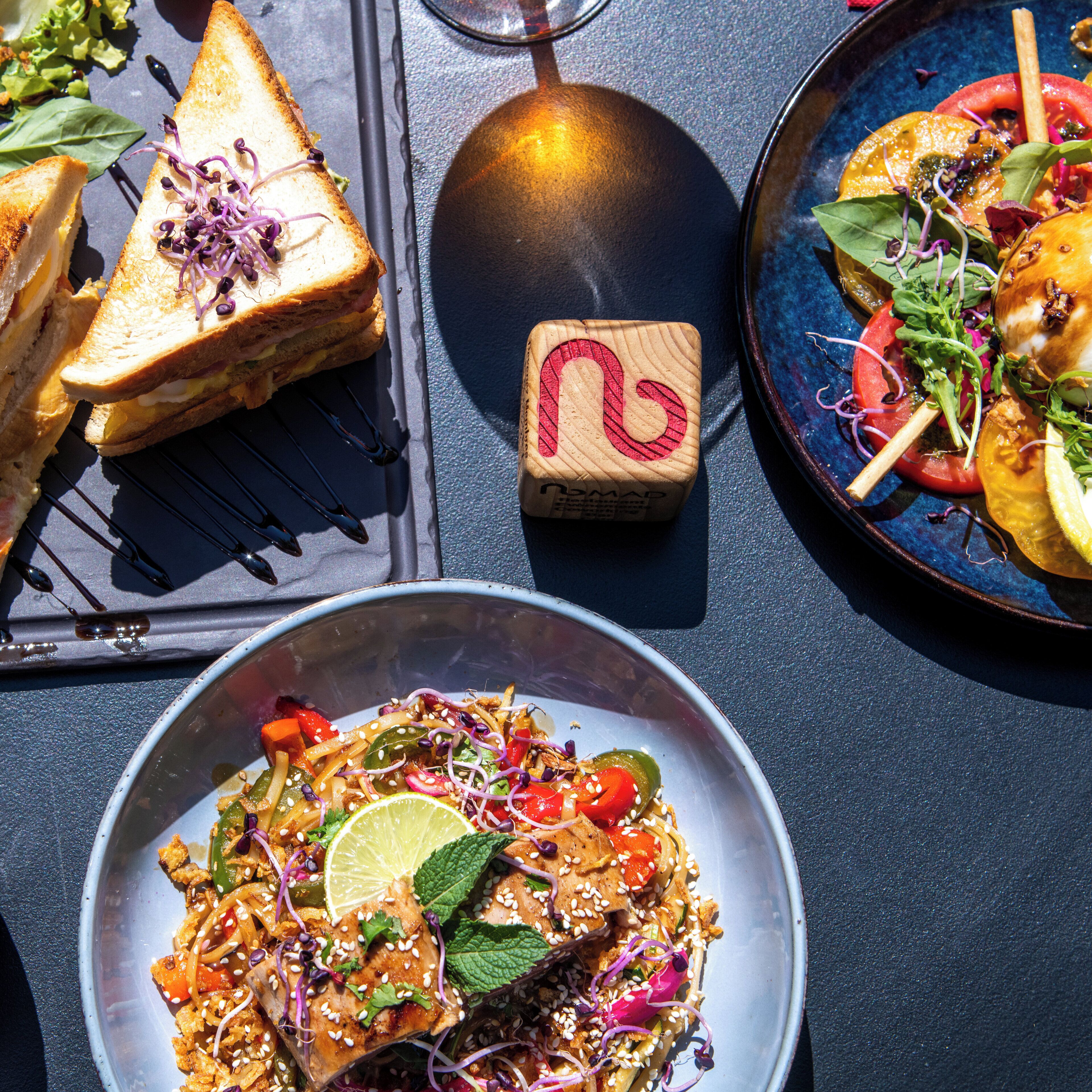 A table with a variety of dishes including a sandwich, a bowl of salad, and a plate with a slice of tomato.