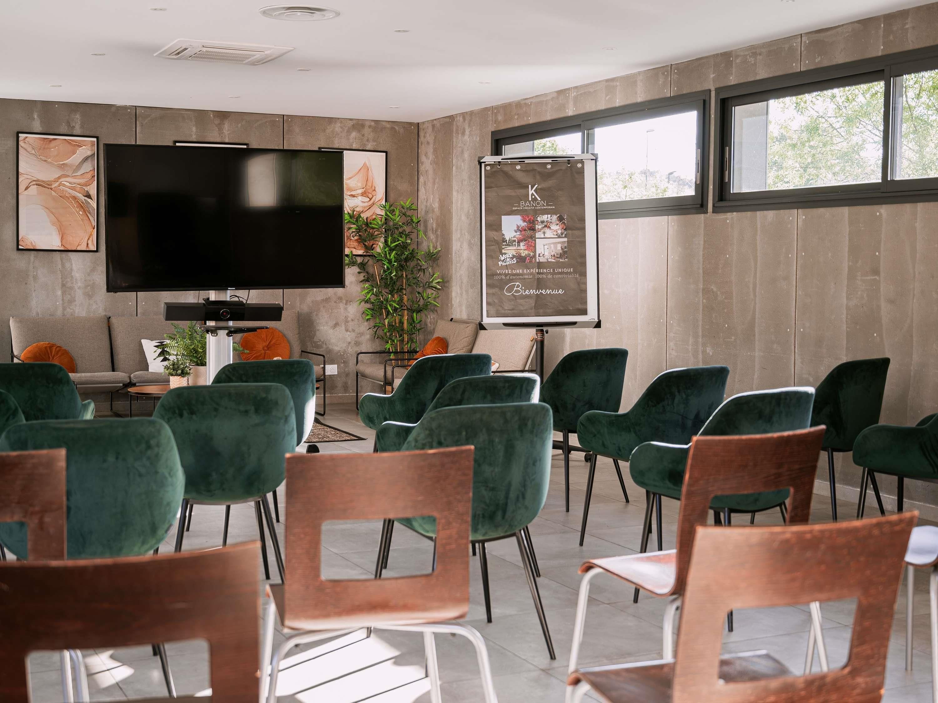 A conference room with a large flat-screen TV, green chairs, a whiteboard, and a poster on the wall.