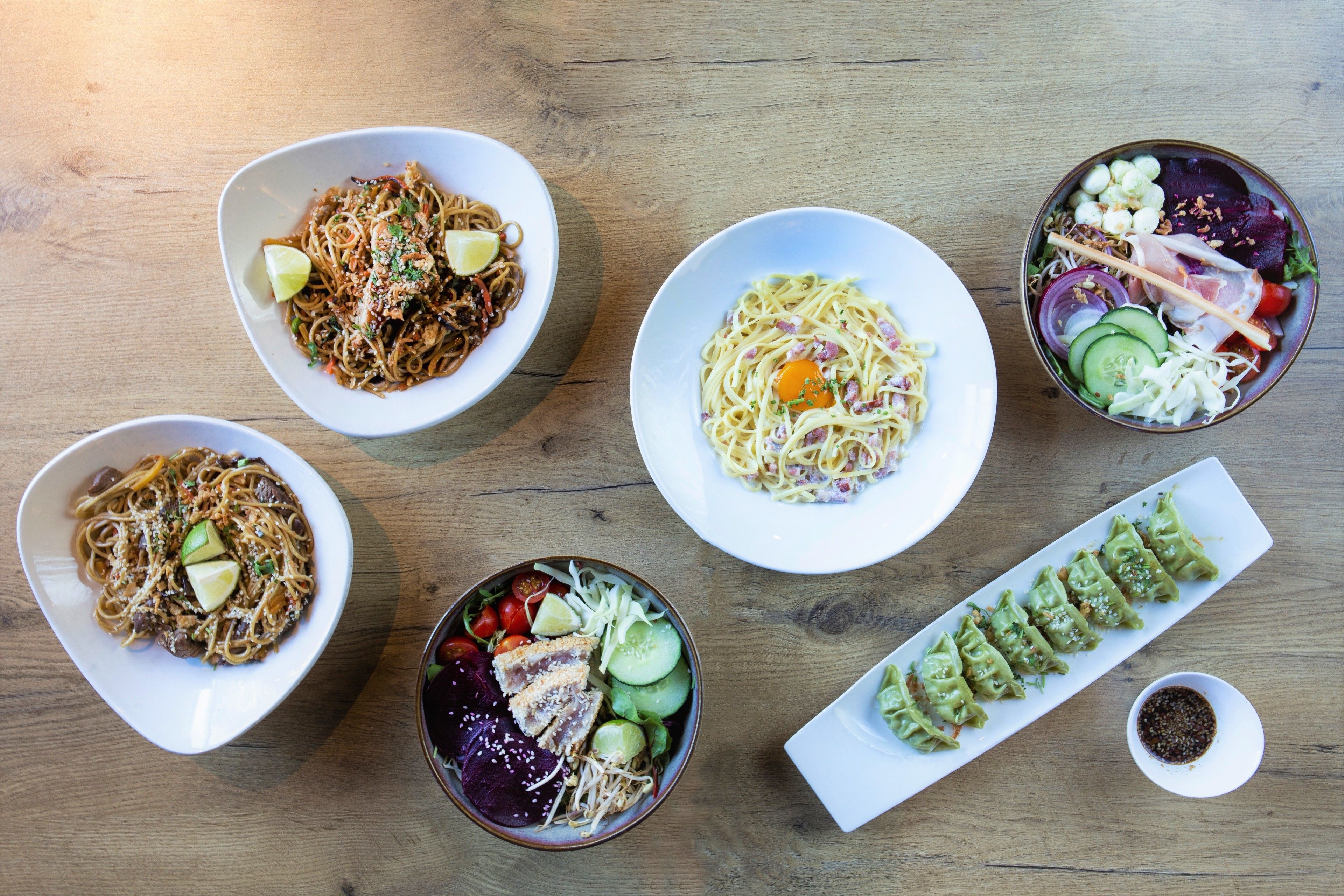 A wooden table with various dishes including noodles, salads, and sushi.