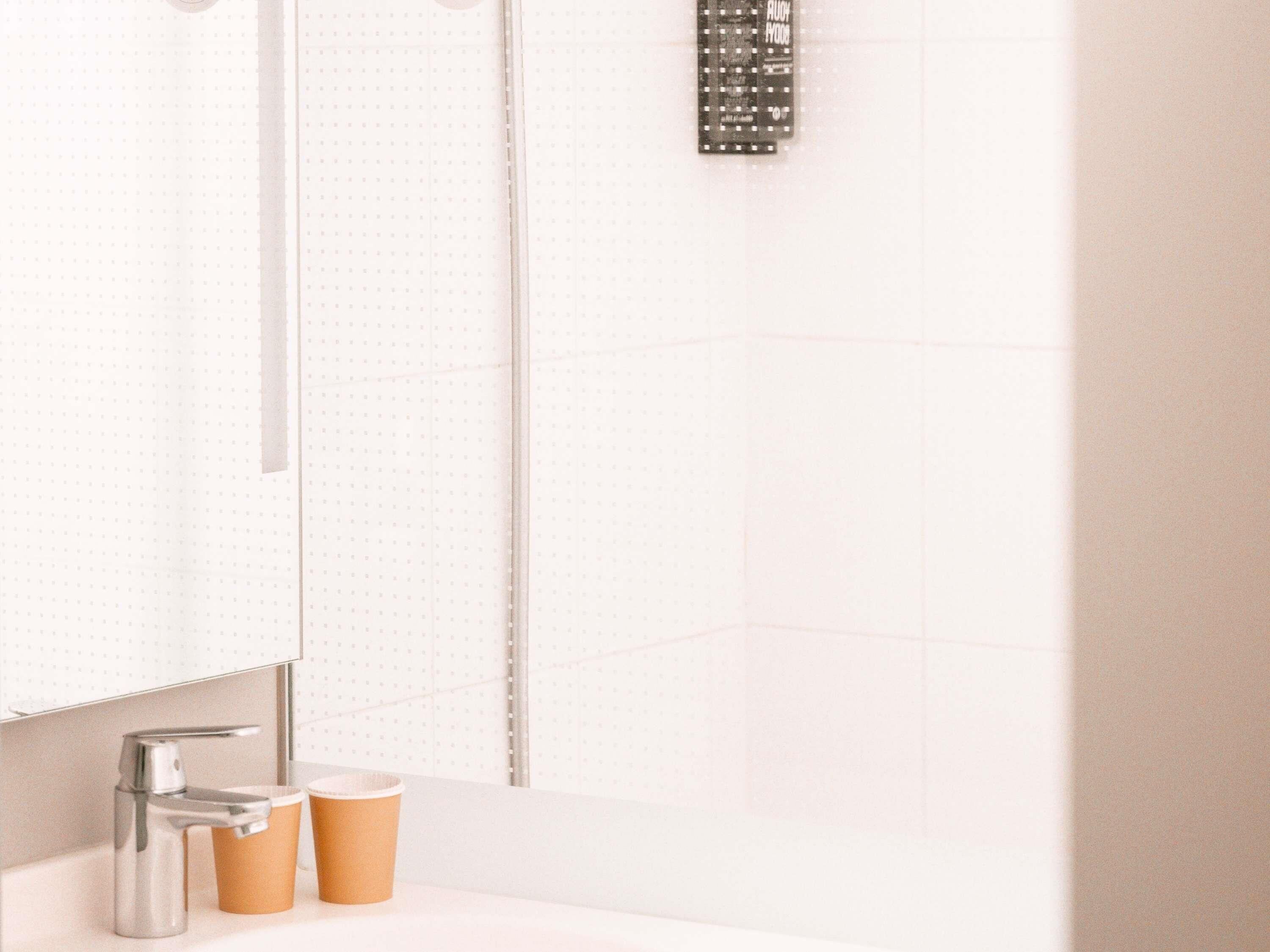A bathroom with a mirror, a sink, a faucet, and two paper cups.