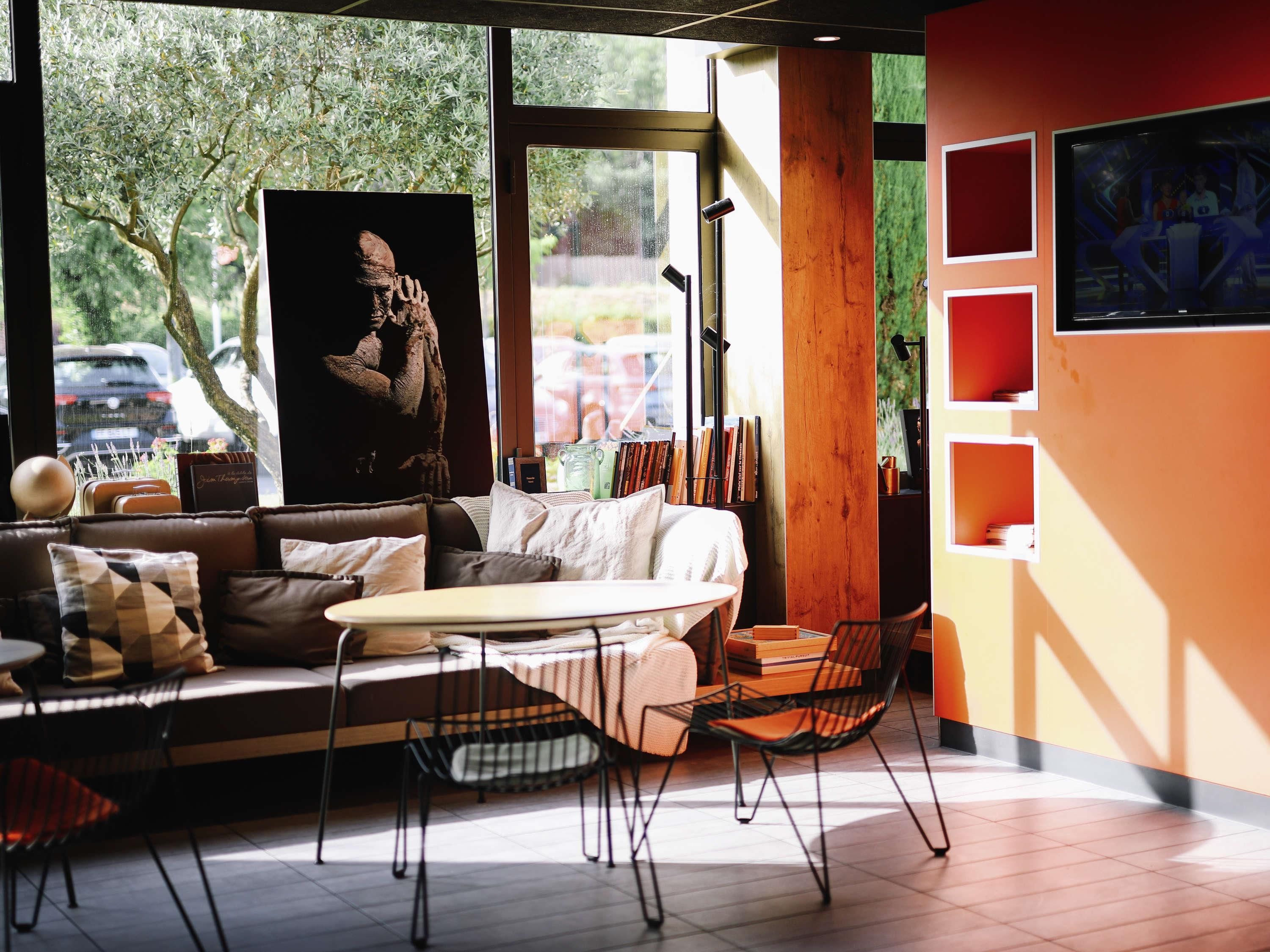 Ein modernes Interieur mit einer Couch, Sesseln, einem Tisch und einem großen Fenster mit Blick auf Bäume und parkende Autos.