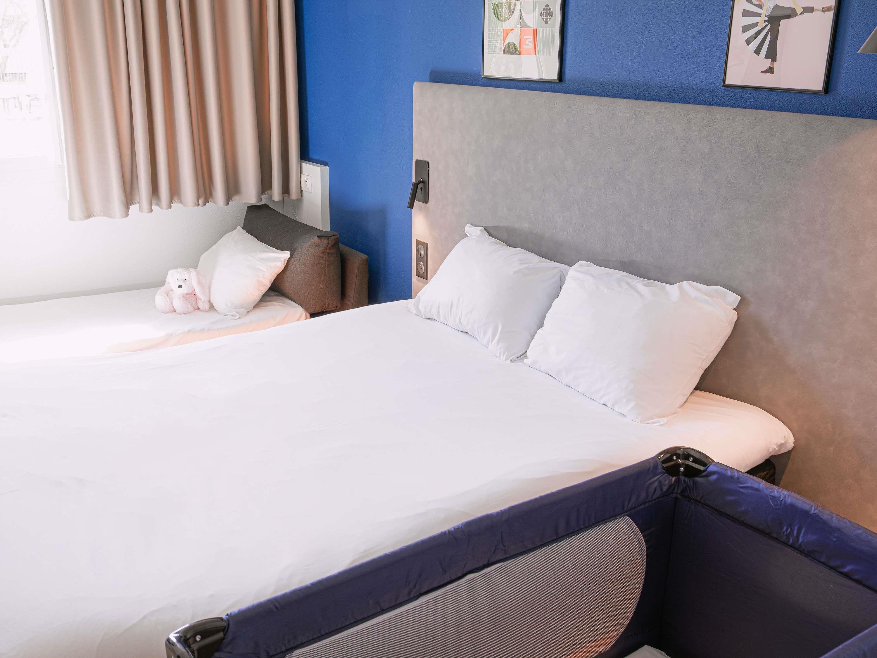 Een hotelkamer met een bed, kussens, een nachtkastje, een lamp en een muur met kunstwerk.
