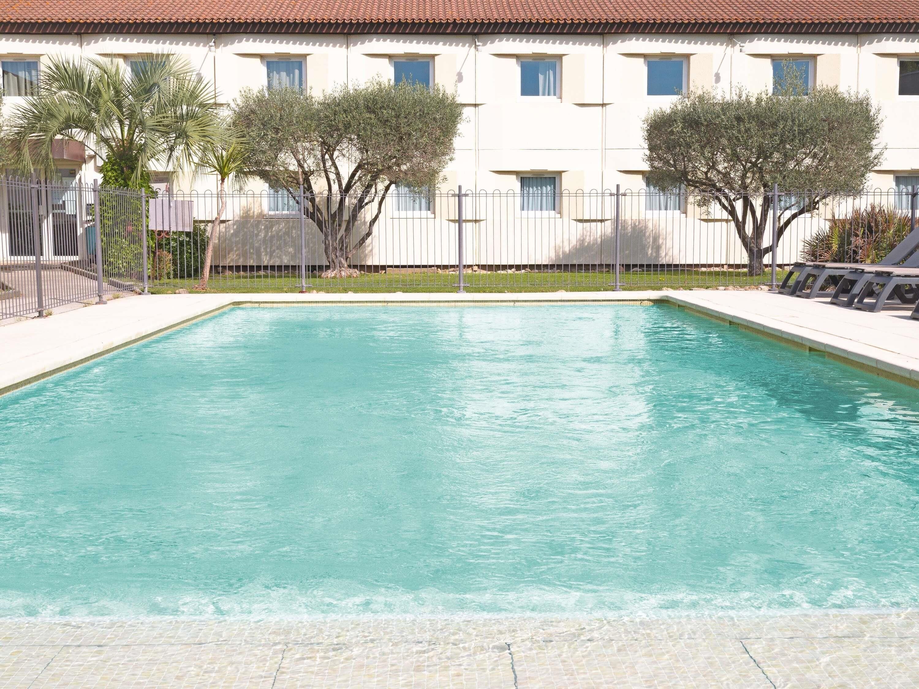 A rectangular swimming pool with clear water, surrounded by a fence and trees.