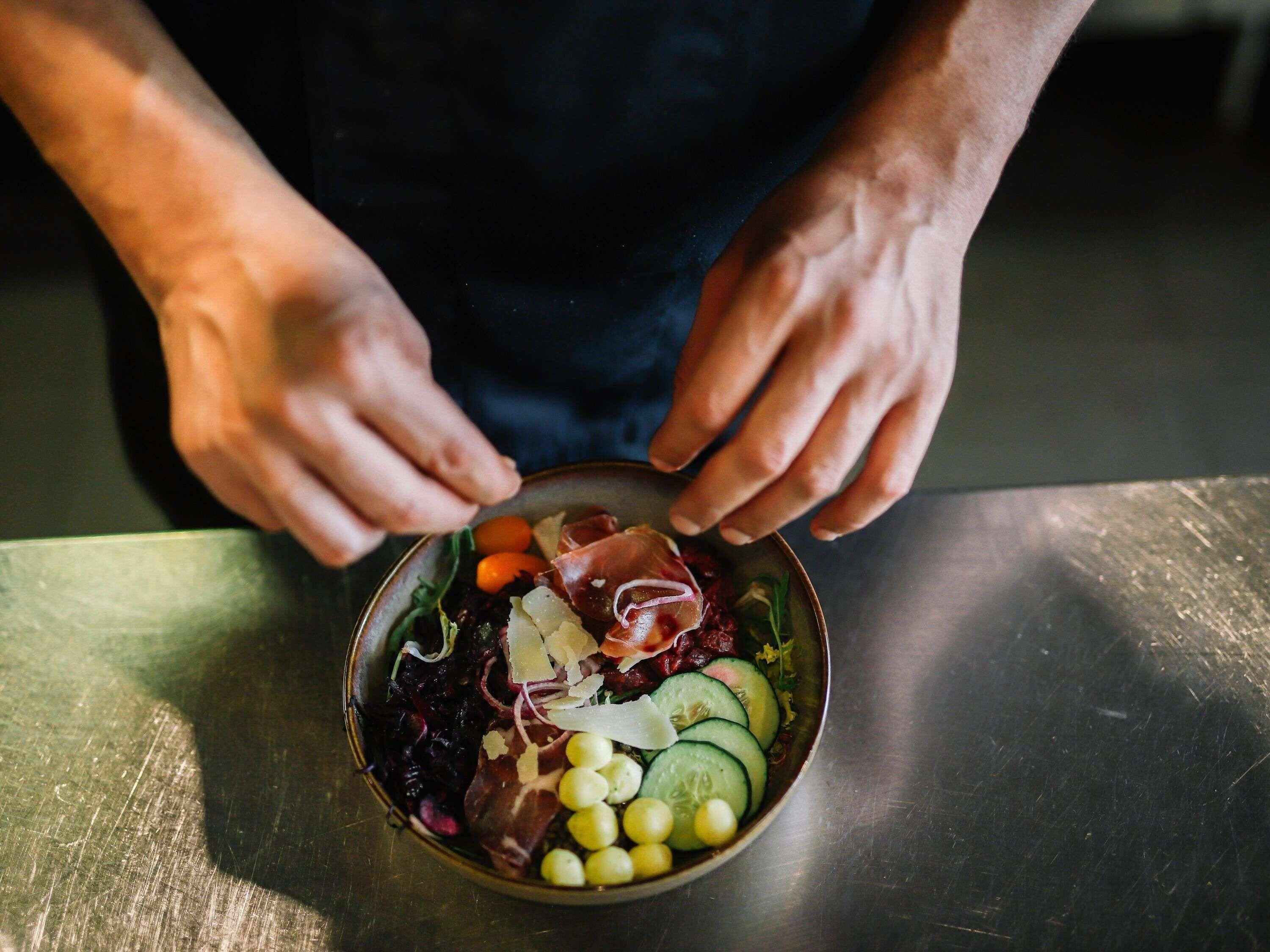 Eine Person hält eine Schüssel mit einem Salat, der verschiedenes Gemüse und Fleisch enthält.