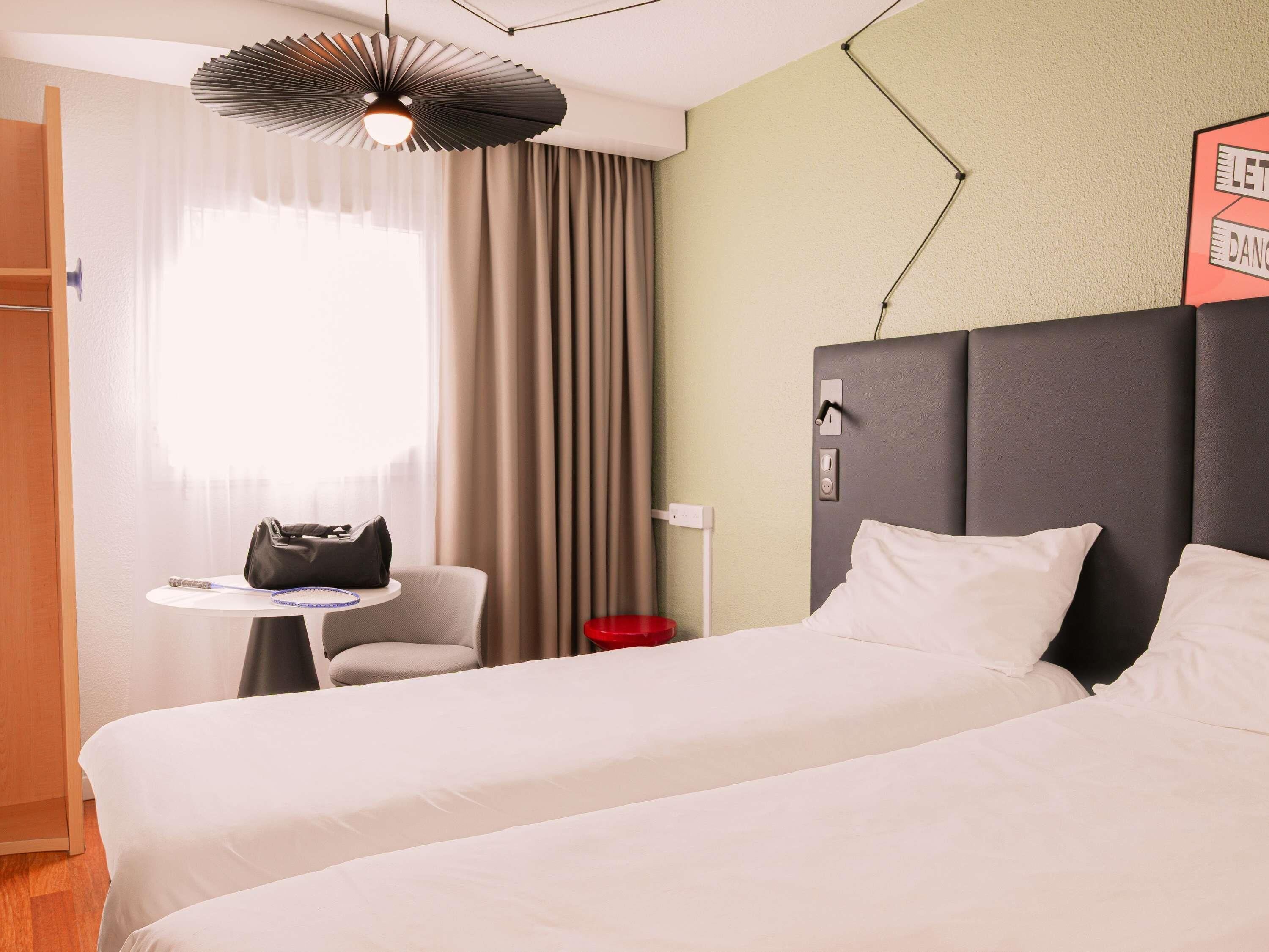 Une chambre d’hôtel comprenant un lit, une table de chevet, une chaise, un bureau, une lampe et une horloge murale.