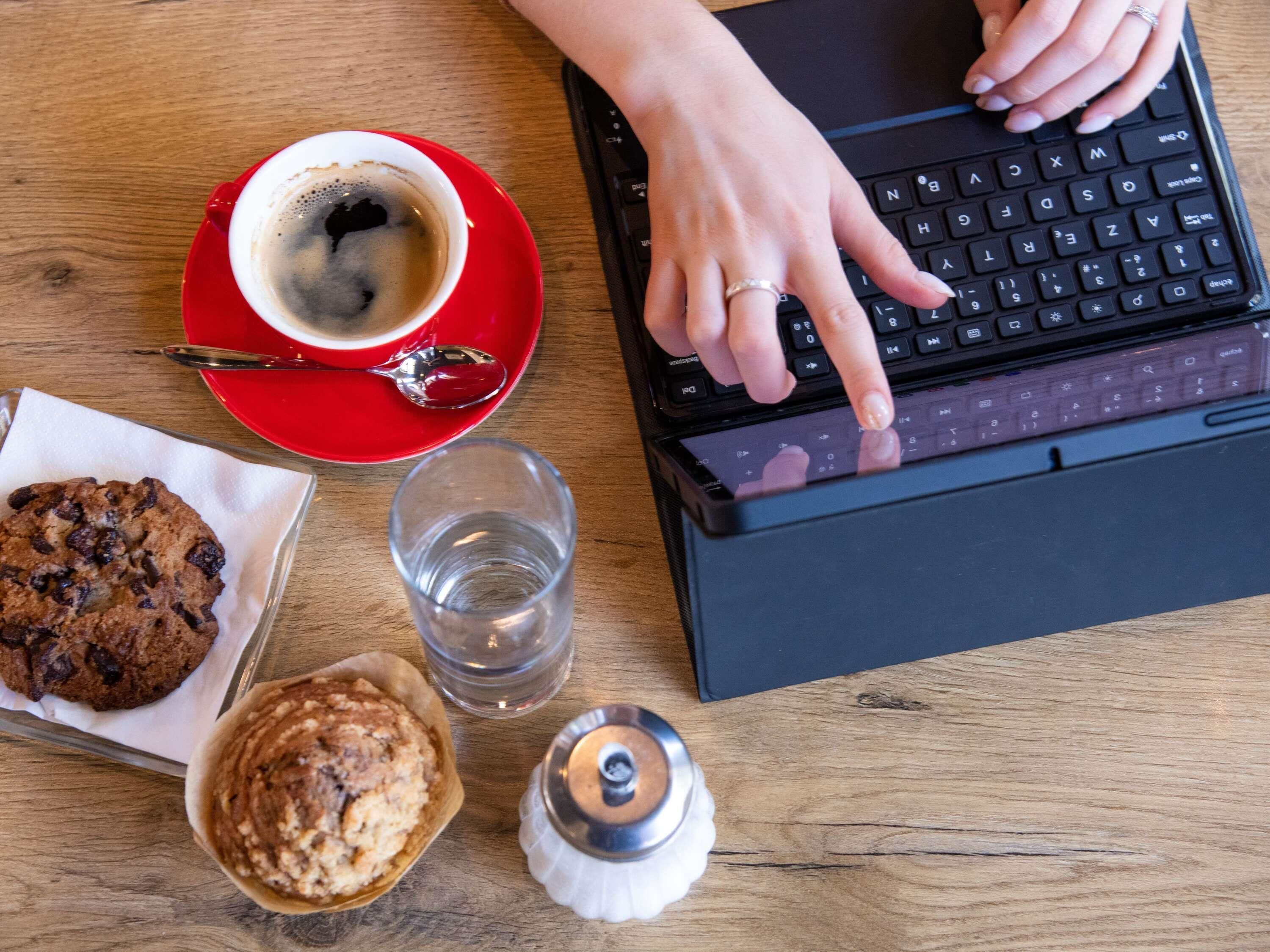 A laptop on a wooden table with a red cup of coffee, a glass of water, and two cookies.