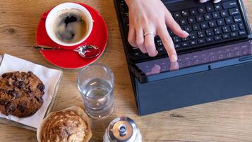 A laptop on a wooden table with a red cup of coffee, a glass of water, and two cookies.