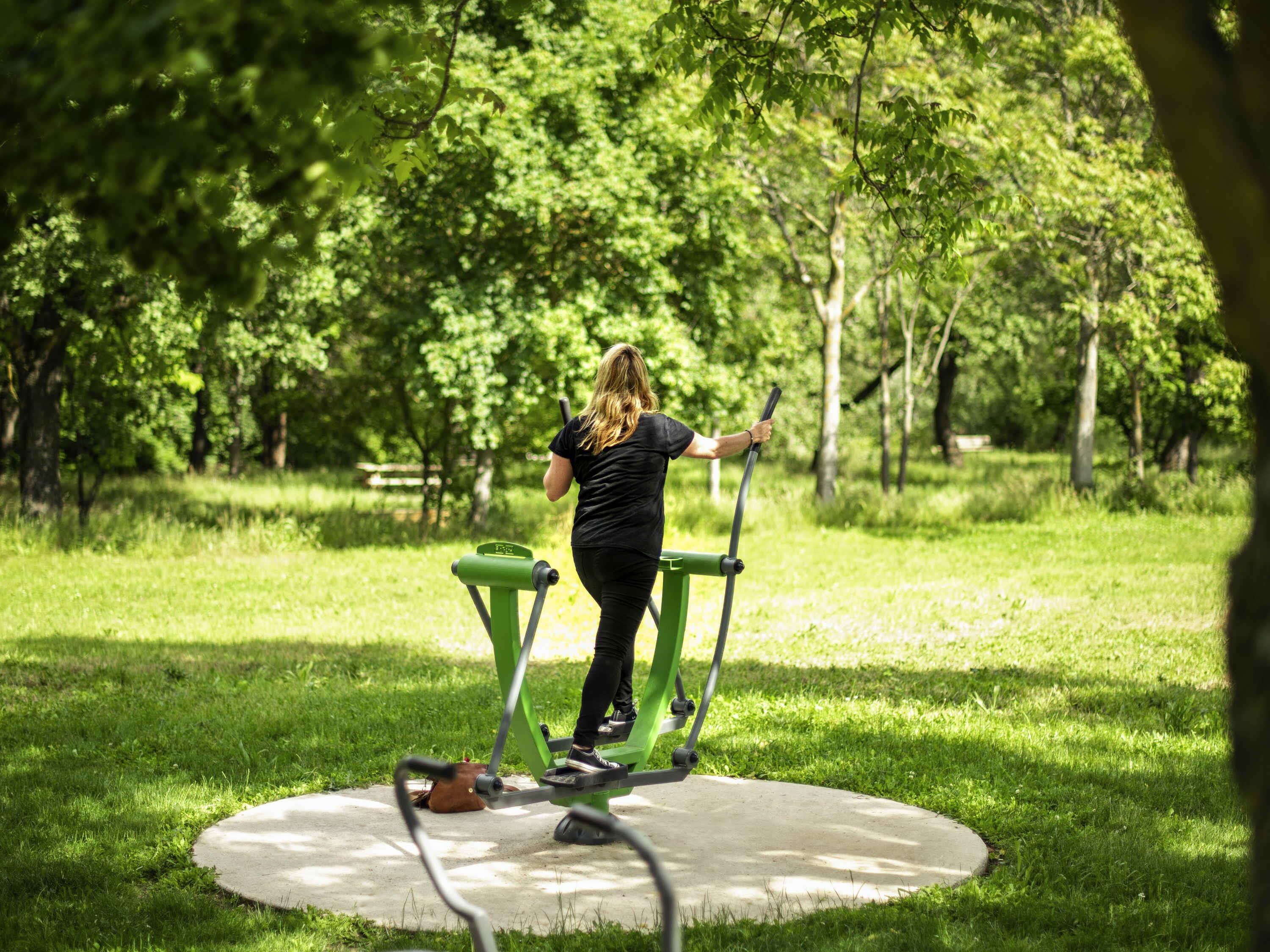 Una persona utilizando una máquina de ejercicios al aire libre en un parque con árboles de fondo.