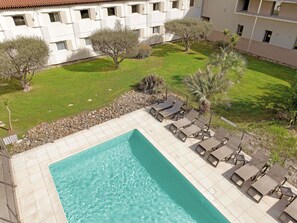 A pool with lounge chairs, a grassy area, and a building with multiple windows. - Ibis Aix en Provence Hotel (Aix-en-Provence)