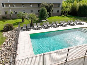 A swimming pool with lounge chairs, a fenced area, and a building in the background. - Ibis Aix en Provence Hotel (Aix-en-Provence)