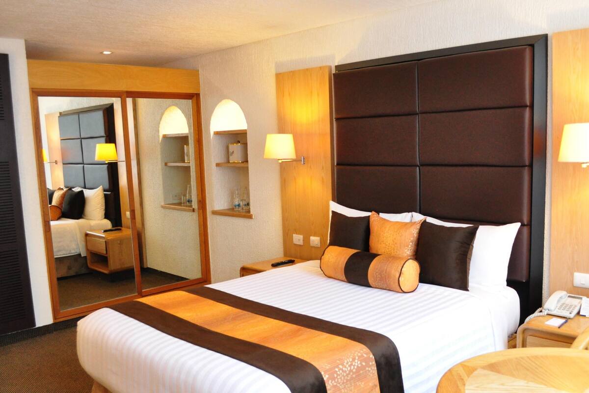 Une chambre d’hôtel avec un grand lit, des tables de chevet, un bureau avec un téléphone et un miroir.