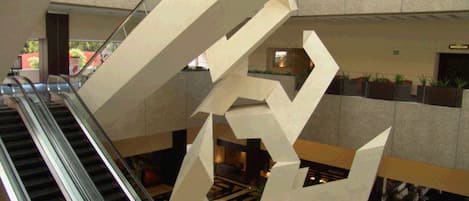 Vista del interior de un edificio con una escalera mecánica y una gran escultura geométrica.