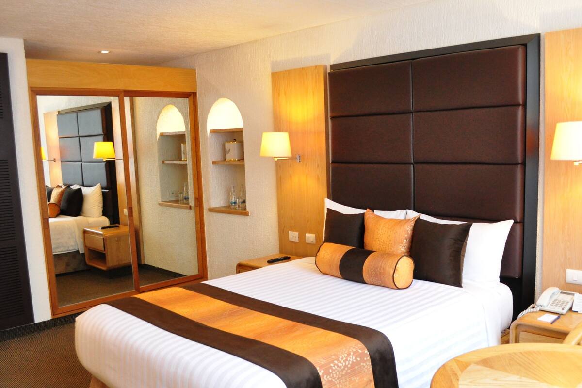 Une chambre d’hôtel avec un grand lit, des lampes de chevet, un miroir, une table de chevet et une chaise.