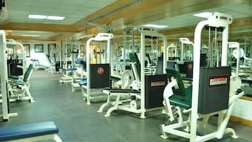 A gym with various exercise machines, benches, and mirrors.