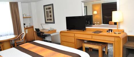 Una habitación de hotel con cama, escritorio, silla, televisor y espejo.