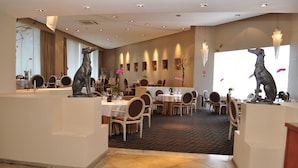 Un restaurante con mesas redondas, sillas y estatuas decorativas de perros.