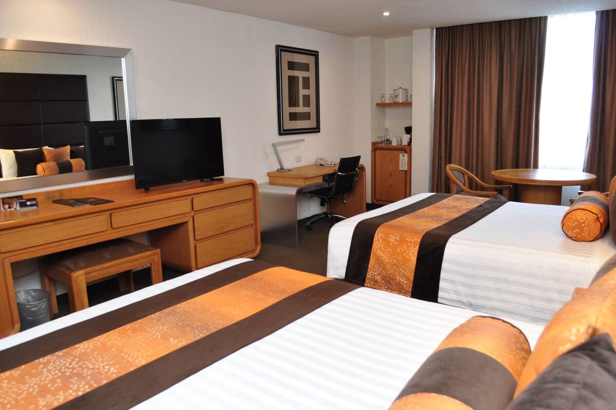Une chambre d’hôtel avec deux lits, un bureau avec un ordinateur, une chaise, une télévision et une petite table.