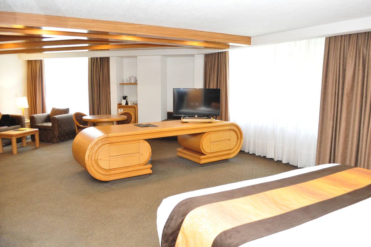 Une chambre d’hôtel avec un grand lit, un bureau en bois avec un téléviseur à écran plat, un canapé et une petite table.