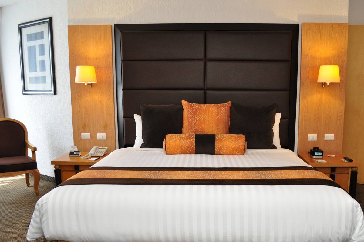 Une chambre d’hôtel avec un grand lit, deux tables de chevet, une chaise et un tableau encadré au mur.