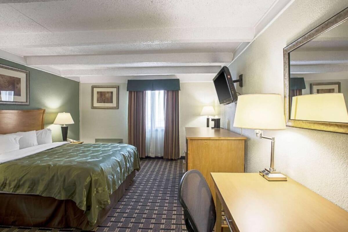 A hotel room with a bed, desk, chair, TV, and a window with curtains.