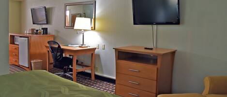 A hotel room with a bed, a desk with a chair, a television, a mirror, and a dresser.