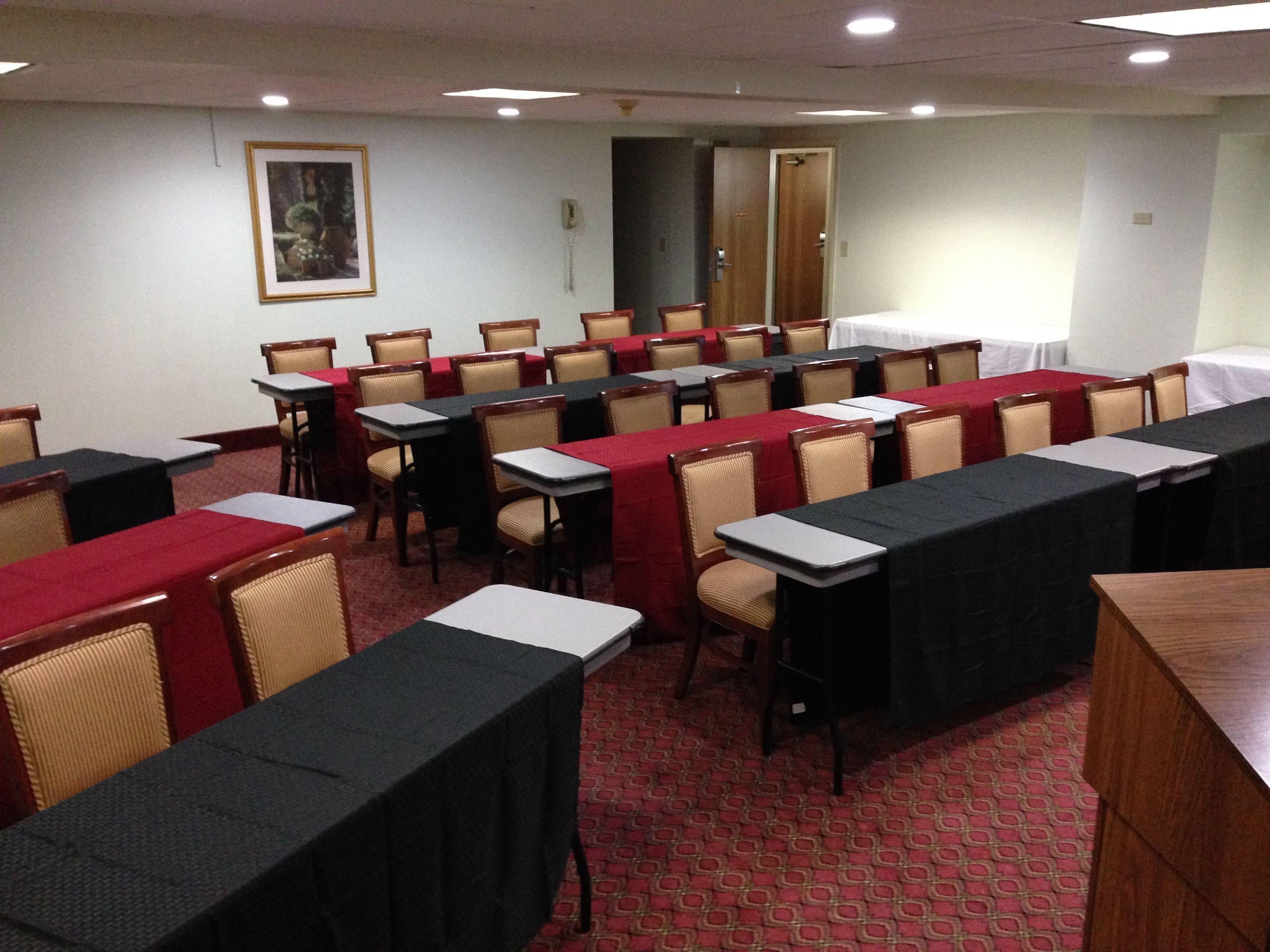 A conference room with rows of tables and chairs, a painting on the wall, and a door in the background.