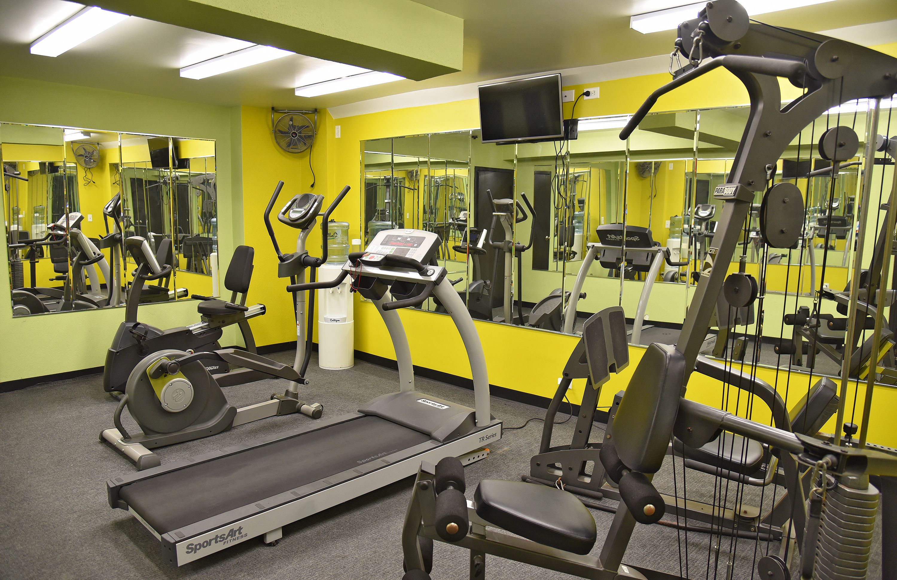 Ein Fitnessstudio mit Trainingsgeräten, Spiegeln und einem Fernseher.