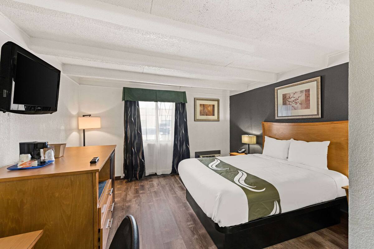A hotel room with a bed, a desk, a TV, a lamp, and a window with curtains.