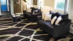 A hotel lobby with two dark sofas, patterned throw pillows, a patterned carpet, and a staircase leading to another level. - Quality Inn & Suites Council Bluffs - Omaha East (Council Bluffs)