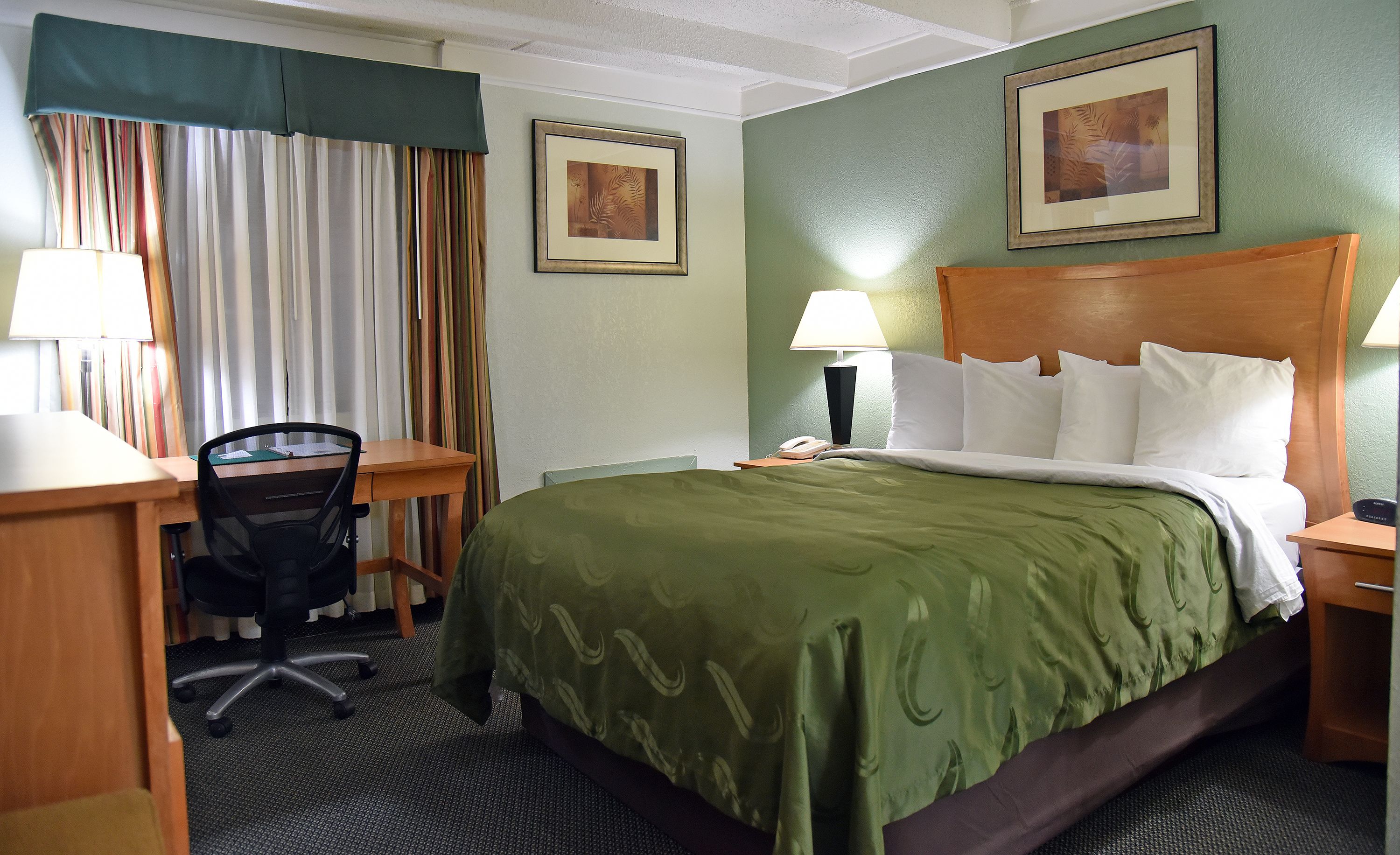 A hotel room with a bed, desk, chair, and two bedside tables with lamps.