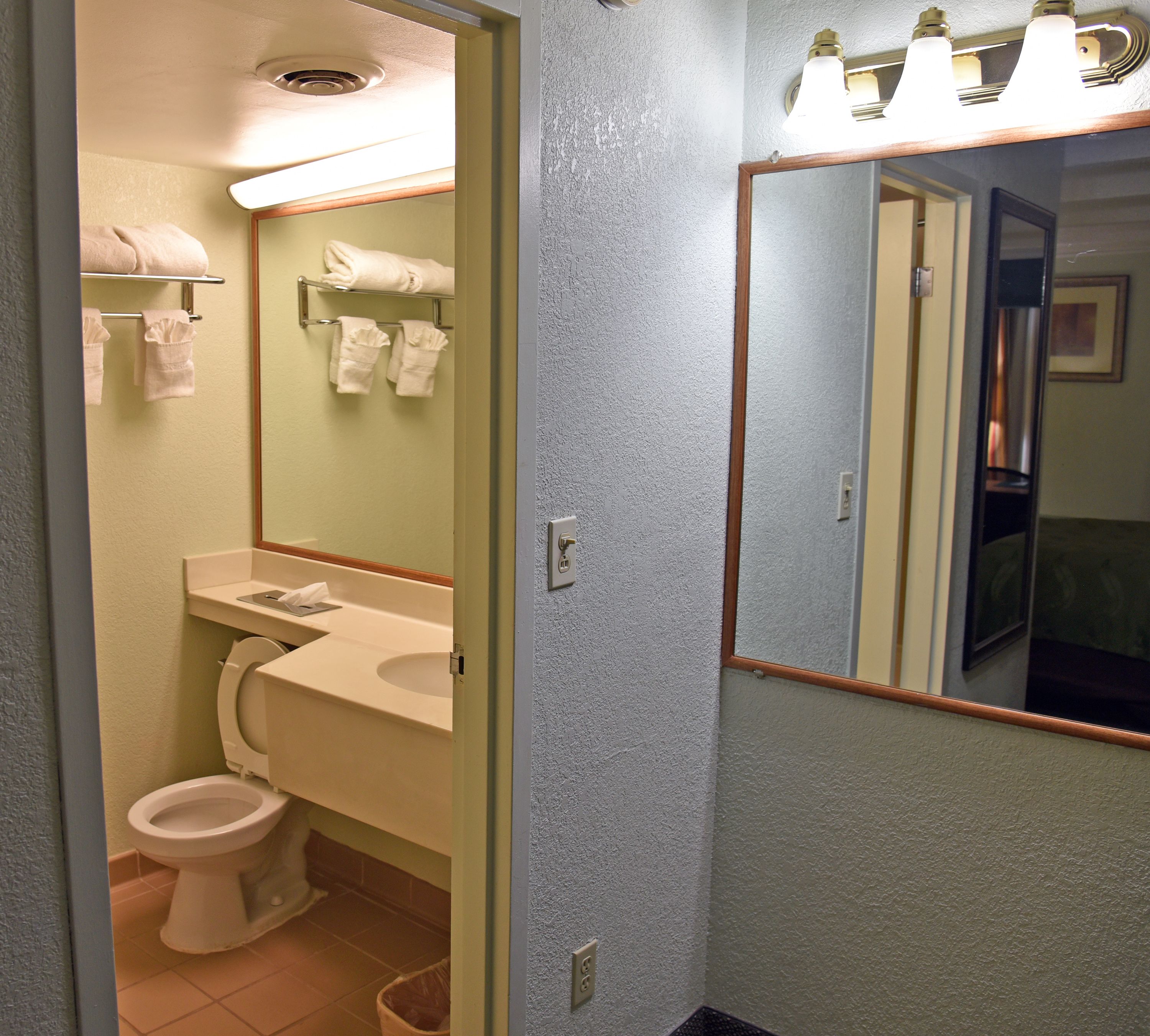 Une salle de bain avec des toilettes, un lavabo et un miroir. Des serviettes sont suspendues sur un porte-serviettes et il y a une poubelle.